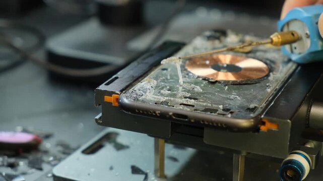 Close up of smartphone repair technician using a rotating brush to remove old adhesive from the phone housing before replacing broken rear glass, smartphone repair and maintenance