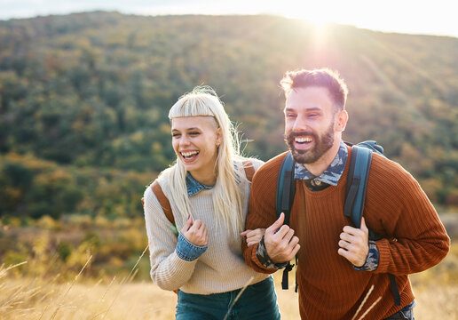 Hiking couple, young man and woman enjoys nature with trekking backpacks  in a lush forest during a sunny day