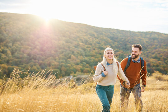 Hiking couple, young man and woman enjoys nature with trekking backpacks  in a lush forest during a sunny day
