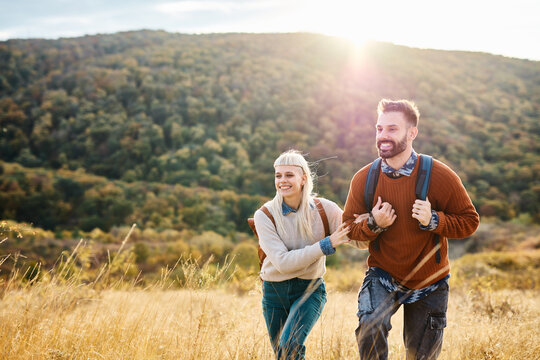 Hiking couple, young man and woman enjoys nature with trekking backpacks  in a lush forest during a sunny day