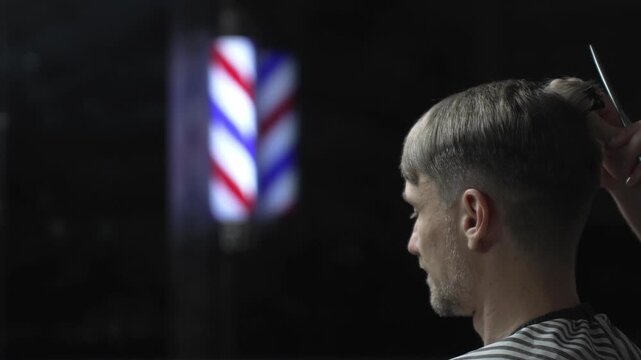 Professional barber grooming male client's hair with scissors, vintage barber pole framing traditional barbershop background