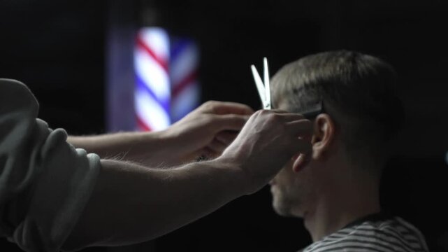 Professional barber grooming male client's hair with scissors, vintage barber pole framing traditional barbershop setting