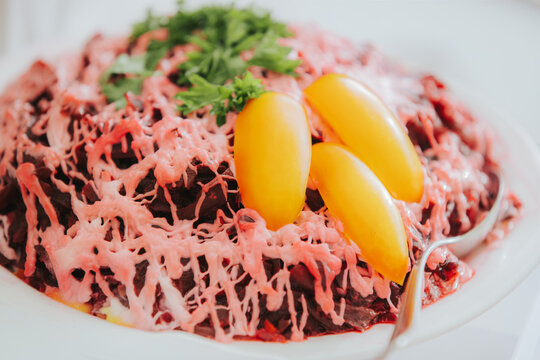 Colorful beet salad topped with shredded cheese and garnished with fresh herbs and yellow cherry tomatoes served on a white plate