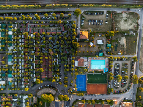 Aerial view of a holiday resort featuring rows of bungalows, a swimming pool, sports courts, and parking areas surrounded by trees in Porto San Giorgio, Marche, Italy.