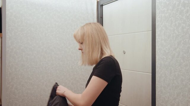 Woman in entryway adjusting jacket, contemplative posture, neutral apartment setting, checking collar and pockets, intimate pause before departure, cinematic soft light and subdued tone