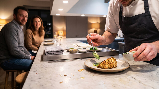 Chef Finishing a Plate at an Open Chefs Counter in Front of Seated Guests, Tasting Menu Service, Interactive Fine Dining, Restaurant Experiential Design