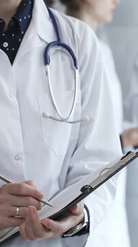 Medical professional writing on clipboard with stethoscope, a doctor and female assistant collaborating in a clinic, discussing patient data and healthcare information