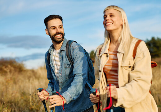 Hiking couple, young man and woman enjoys nature with trekking poles in a lush forest during a sunny day