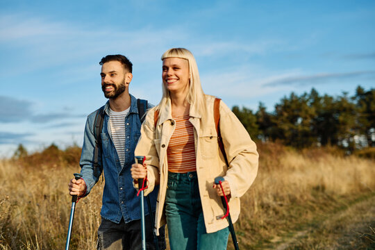 Hiking couple, young man and woman enjoys nature with trekking poles in a lush forest during a sunny day