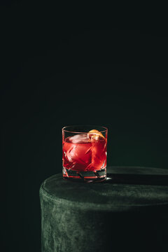 Red cocktail with ice and orange peel in low key light