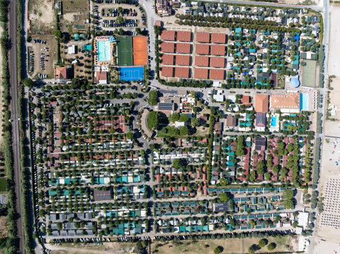 Aerial view of a large camping resort featuring rows of mobile homes, swimming pools, sports courts, and lush trees, located near the beach in Porto San Giorgio, Marche, Italy.