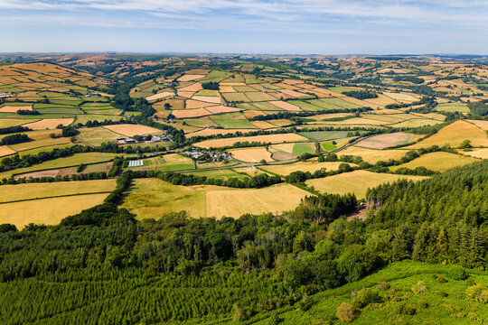 Aerial view of rolling farmland and forested hill slopes, mosaic of harvested crops and grazing pasture defining rural land use across undulating terrain