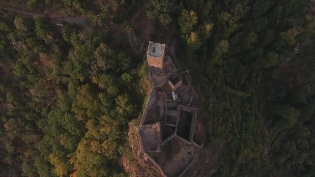 Stunning aerial perspective showing the ruins of Saint Ulrich Castle at sunset. The medieval fortress is nestled on a hill surrounded by forest