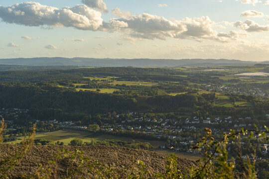 View of the rolling hills and lush green landscape surrounding the town, with scattered houses, fields, and a soft sunset sky in Konigswinter, North Rhine-Westphalia, Germany.