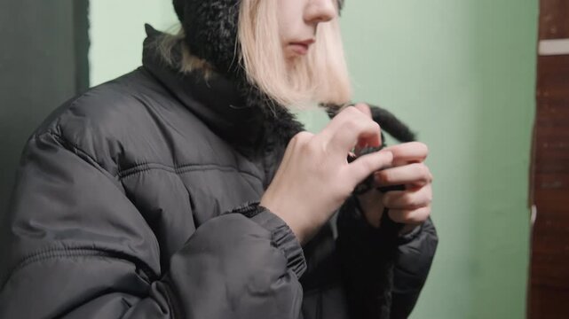 Indoor scene of woman preparing for cold weather. Detailed shot of woman arranging clothing for winter outing. Intimate closeup of woman adjusting scarf and hood before outdoor winter travel