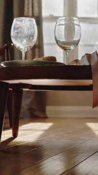 Vertical video: Rising camera revealing coffee table at window, showing two wine glasses and plate