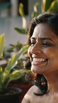 Vertical video: Turning shot, woman in sleeveless top laughing reaching pots on balcony, copy space
