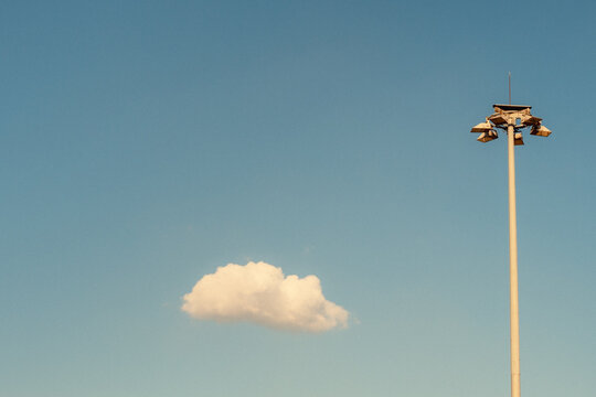 Stadium floodlight pole above solitary cloud in blue sky