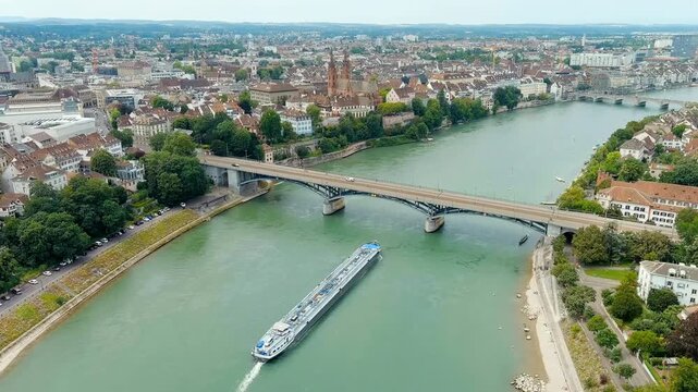 Basel, Switzerland. Wettstein Bridge, a long steel and concrete road structure spanning the Rhine River, with a large tanker cargo barge passing beneath and traffic flowing across its deck. Drone foo
