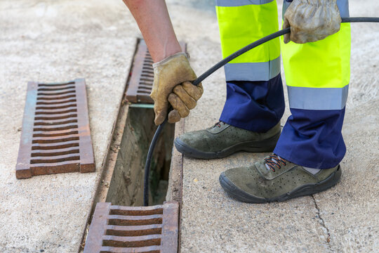 Sewer worker unclogging blocked drain grate with water jetting hose.