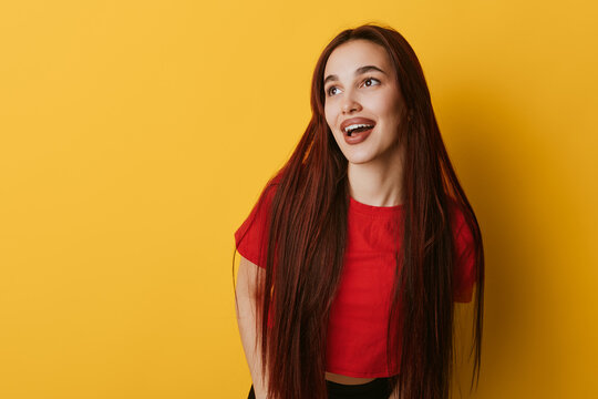 Young woman with long hair wearing red shirt smiling and looking away on yellow background. Portrait of happy female with casual style and natural expression in studio.