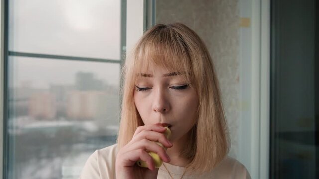 Happy woman trying small dish near window. Smiling woman experiencing culinary sample in sunlight at home kitchen. Cheerful woman enjoying taste test in cozy kitchen with natural bright lighting