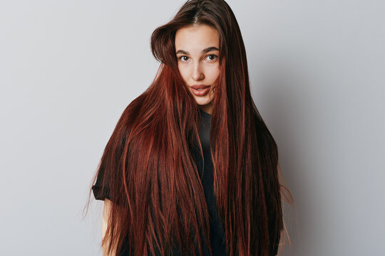 Woman with long straight hair and natural makeup posing against white background. Young female model with red hair wearing black t shirt looking at camera with soft expression.