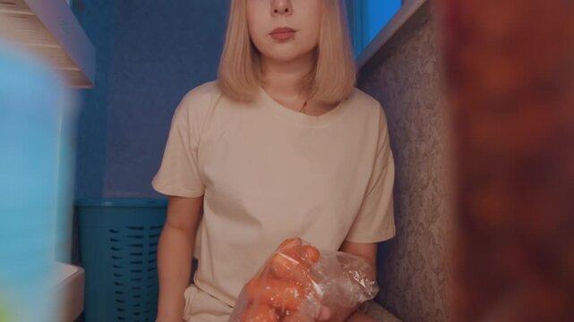 White woman holding tomatoes in fridge, pausing to decide recipe, shorts and shirt, apartment kitchen, amateur chef testing ideas, gentle blue lighting, contemplative expression, recipe planning