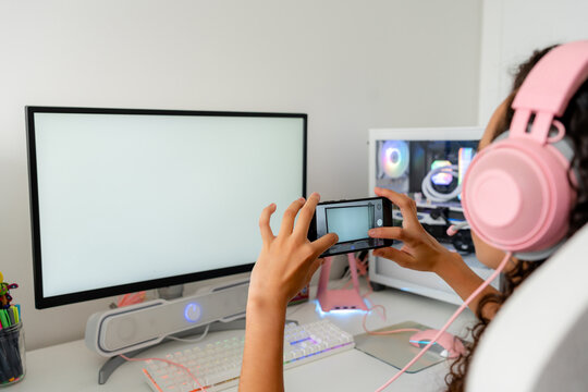 Young woman gamer with smartphone at desktop computer