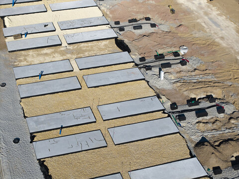 Aerial view of the BESS battery energy storage system construction site with concrete foundation slabs, electrical conduits, and sandy ground in Poland.