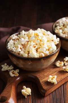 Two bowls of freshly popped popcorn served on a rustic wooden board with a dark background