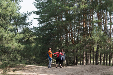 Fototapeta premium Three young hikers hold hands while standing together in a circle among tall pine trees during an outdoor hiking trip.