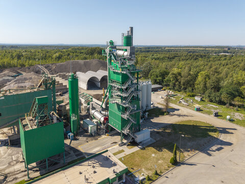 Aerial view of Masfalt Sp. z o.o. WMB asphalt plant with green silos, machinery, and gravel piles surrounded by forest in Dabrowa Gornicza, Wojewodztwo slaskie, Poland.