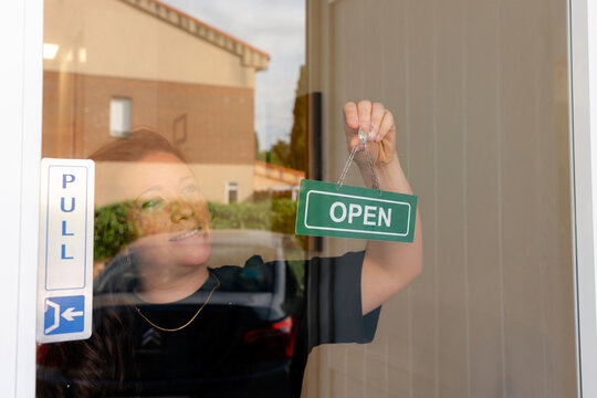 Woman display open sign on small business glass door