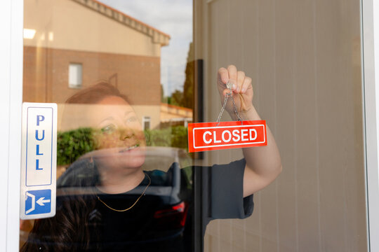 Woman placing closed sign on storefront glass door
