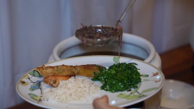 serving feijoada onto a plate, Brazilian food buffet