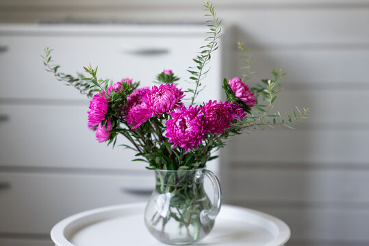 Pink flower bouquet in glass pitcher on white table