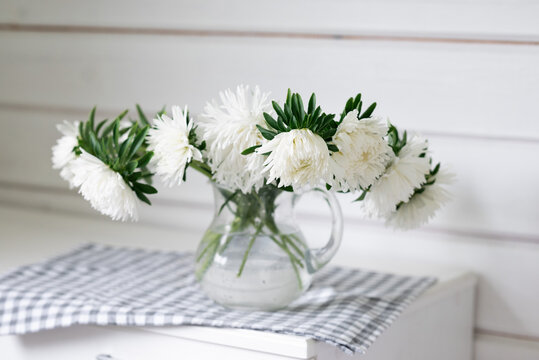 White flower bouquet in glass pitcher on checkered cloth