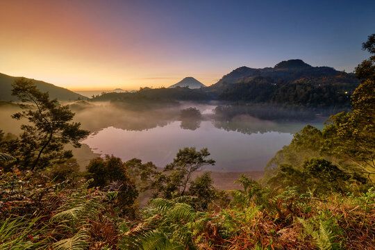 View of Telaga Warna in Dieng Park at sunrise with mist over the water and surrounding mountains in Kejajar, Central Java, Indonesia.