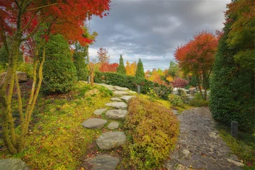 Fotobehang Badkamer Scenic path made of stepping stones and a paved rock walkway winding through a traditional Japanese garden with vibrant red maples and trimmed green bushes. Peaceful botanical park environment design.  © GIS