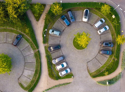Aerial view of a circular parking lot with parked cars arranged around a central tree, surrounded by manicured hedges and paved walkways in Sopot, Pomeranian Voivodeshi, Poland.
