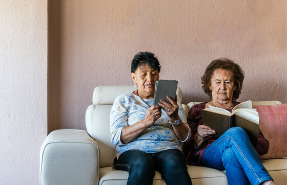 Senior women read ebook and book together at home