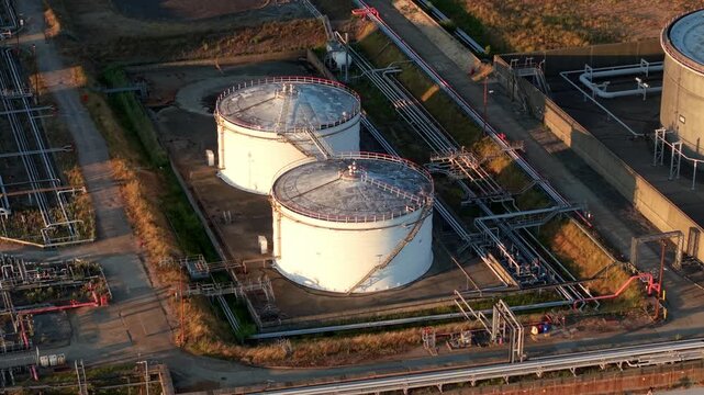 Aerial view of white cylindrical oil storage tanks at the LPG LNG terminal with industrial piping and sunset lighting in Hamble-le-Rice, England, United Kingdom.