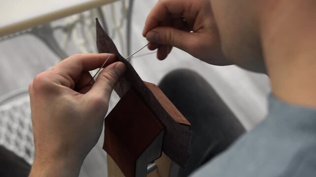 Leather craftsman hand stitching genuine leather with needle and thread using a stitching pony in his workshop