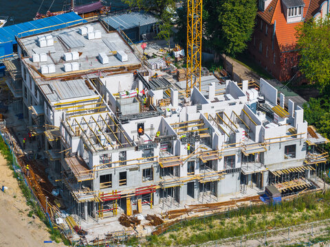 Aerial view of a construction site with workers, a yellow tower crane, and concrete structures in progress in Gdansk, Pomeranian Voivodeship, Poland.