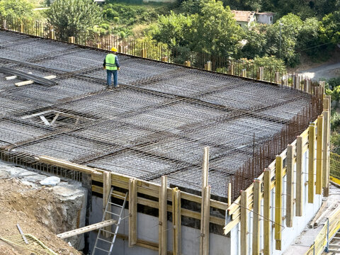 View of a construction worker in a high-visibility vest standing on a steel rebar grid for a concrete slab, with wooden formwork and a ladder in Sariyer, Istanbul, Turkiye.