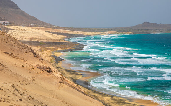 Aerial view of Praia Grande with turquoise waves, golden sand dunes, and rugged coastal hills in Mindelo, Sao Vicente, Cabo Verde.
