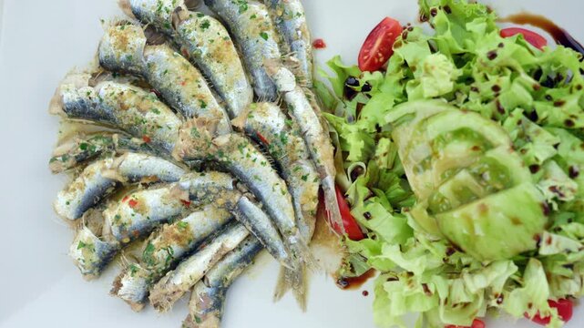Grilled sardines with golden breadcrumbs and green herbs, served alongside fresh lettuce leaves and tomato, creating a healthy meal