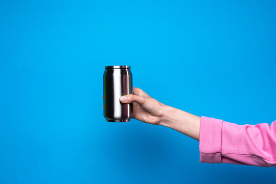 Female hand hold metal drink can on blue background
