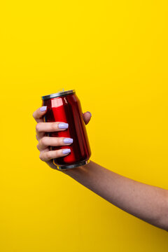 Female hand hold red beverage can on yellow background